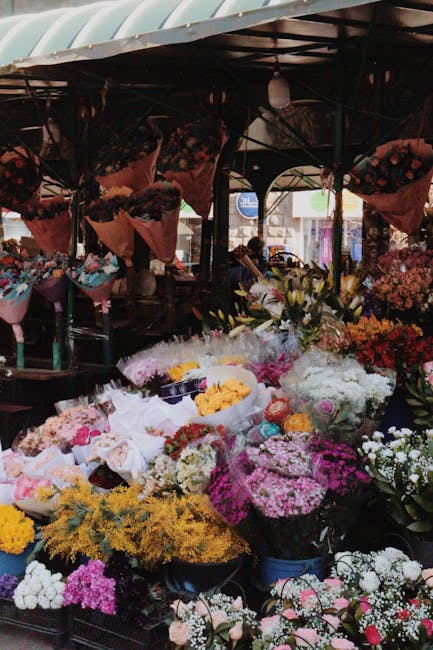 A vibrant display of floral arrangements at a florist shop, showcasing a variety of fresh flowers including bright pink hydrangeas, white begonias, purple hydrangeas, and orange and yellow kalanchoes,