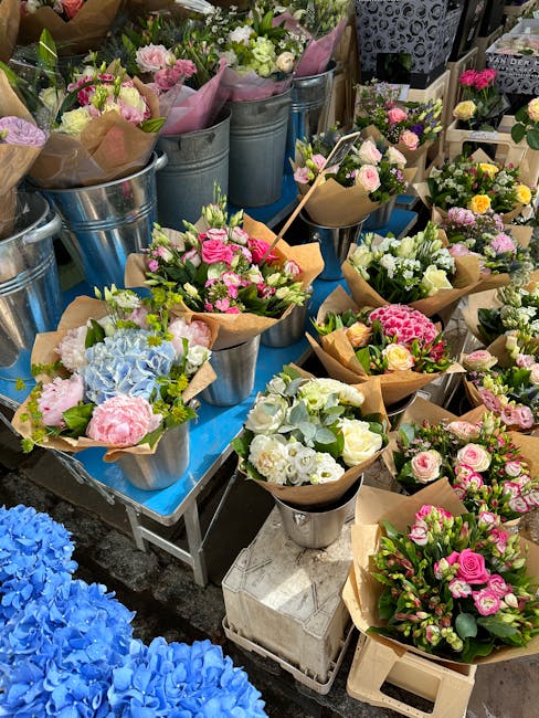 A vibrant display of fresh flowers arranged in bouquets and potted plants at a flower market stall run by floristchalkfarm.co.uk. The arrangement includes a variety of colourful blooms such as white, 